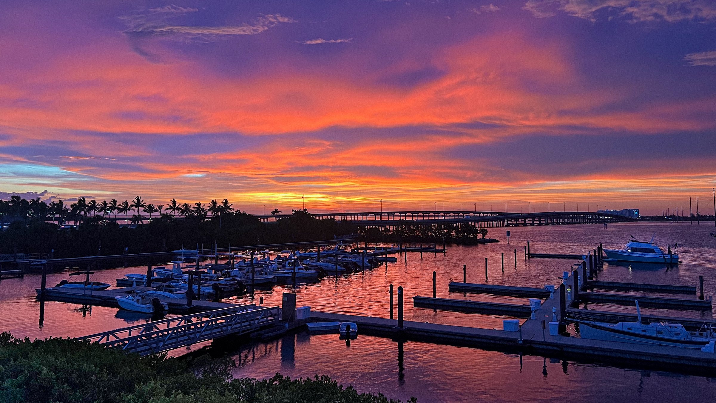 The Punta Gorda marina at Laishley Park under a purple and orange sunset, the US-41 bridge crossing the Peace River in the distance